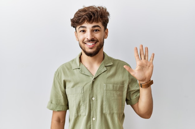 Jeune médecin arabe debout sur un fond isolé montrant et pointant vers le haut avec les doigts numéro cinq tout en souriant confiant et heureux