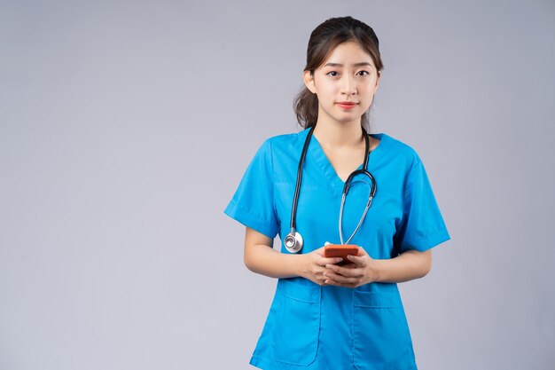 Jeune médecin asiatique avec smartphone sur gris