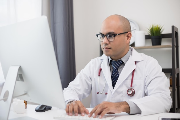 Jeune médecin asiatique travaillant des textos en ligne sur la vidéoconférence du clavier avec l'équipe Close Up Physician in white coat stethoscope travaillant avec ordinateur