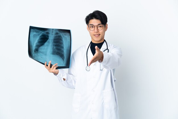 Jeune médecin chinois man holding radiographie isolé sur fond blanc se serrant la main pour conclure une bonne affaire