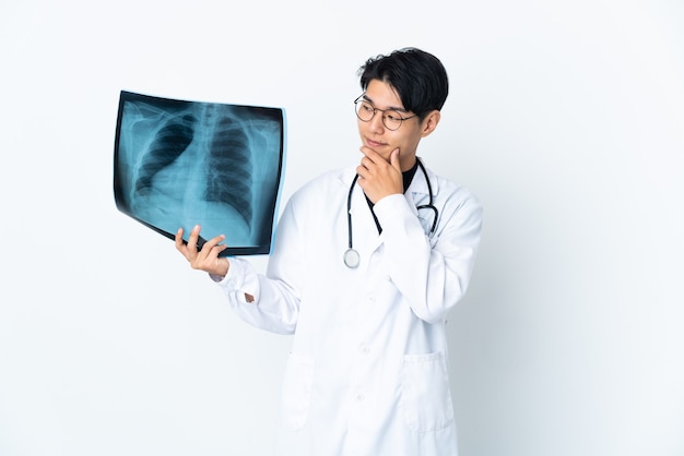 Jeune médecin chinois man holding radiographie isolé sur mur blanc regardant sur le côté et souriant