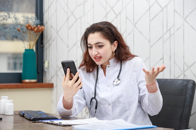 Jeune médecin choqué assis au bureau et regardant le téléphone