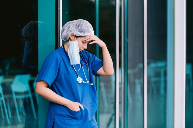 Une jeune médecin en combinaison de protection, en uniforme et en masque, se sent épuisée et inquiète.