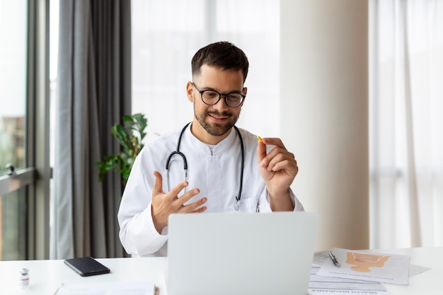 Jeune médecin concentré travaillant sur ordinateur regardant un écran d'ordinateur portable pensant au concept de solution de problème Homme sérieux médecin portant un manteau blanc faisant des recherches en ligne sur le lieu de travail