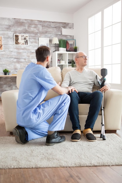 Jeune médecin dans une maison de retraite parlant avec un vieil homme atteint de la maladie d'alzheimer alors qu'il a l'air perdu.