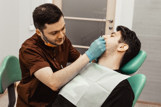 Un jeune médecin dentiste de sexe masculin traite un patient. Manipulations médicales en dentisterie, chirurgie. Santé Équiper le lieu de travail d'un médecin. Dentisterie