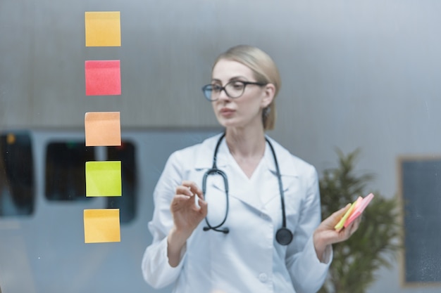 Un jeune médecin élabore un plan stratégique, colle des autocollants colorés sur un verre transparent.