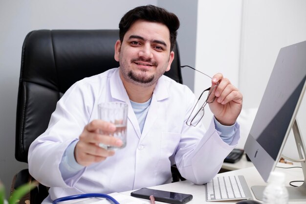 Photo un jeune médecin est assis dans la clinique tenant un verre d'eau à la main