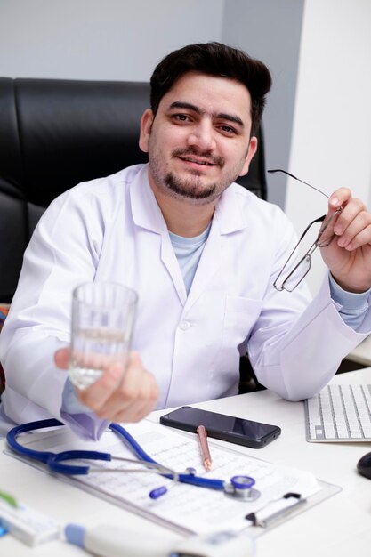 Photo un jeune médecin est assis dans la clinique tenant un verre d'eau à la main