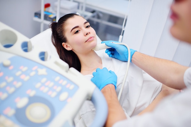 Un jeune médecin fait une échographie de la glande thyroïde à une patiente.