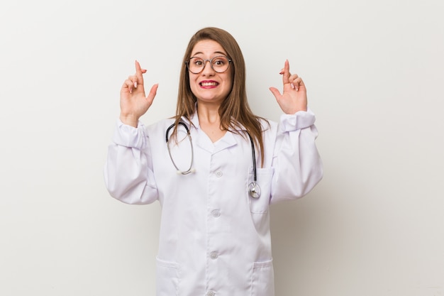 Jeune médecin femme contre un mur blanc croise les doigts pour avoir de la chance
