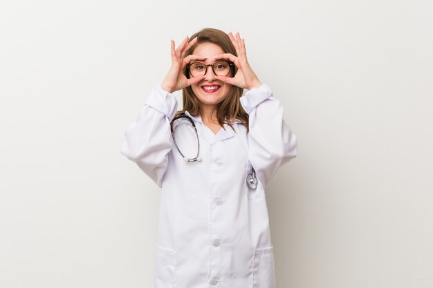 Jeune médecin femme contre un mur blanc montrant un signe correct sur les yeux