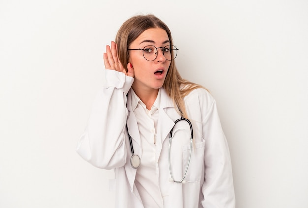 Jeune médecin femme russe isolée sur fond blanc essayant d'écouter un potin.