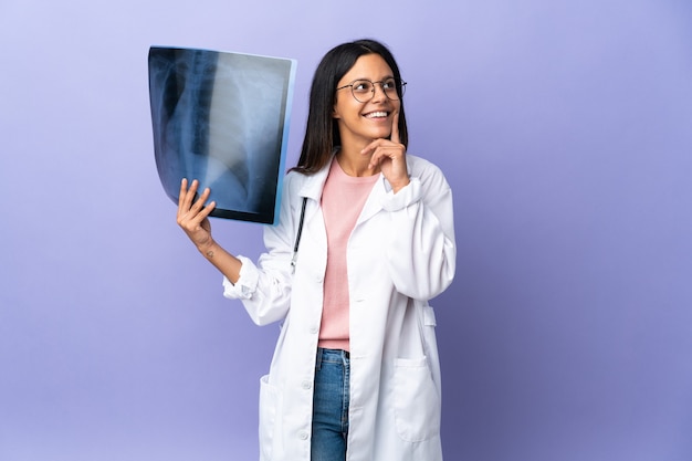 Jeune médecin femme tenant une radiographie en pensant à une idée tout en levant