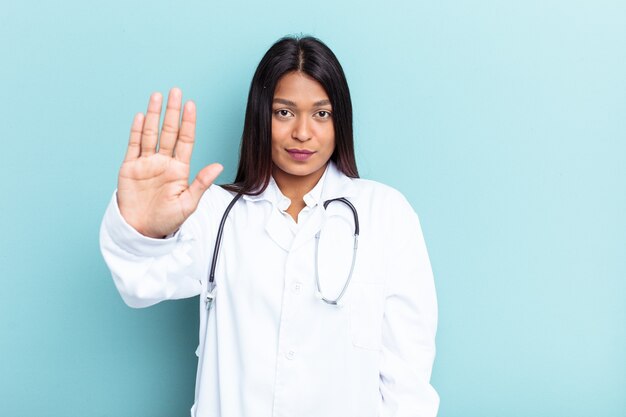 Jeune médecin femme vénézuélienne isolée sur fond bleu debout avec la main tendue montrant un panneau d'arrêt, vous empêchant.
