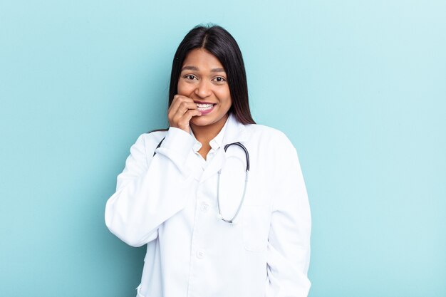 Jeune médecin femme vénézuélienne isolée sur fond bleu se rongeant les ongles, nerveuse et très anxieuse.