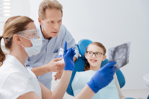 Jeune Médecin De Formation Distinguée Regardant Le Scan Et Tirant Ses Conclusions Pendant Que La Famille Attend Les Résultats