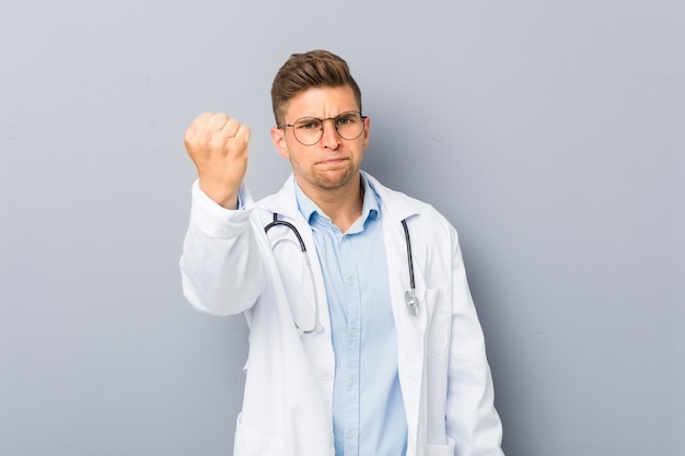 Jeune médecin homme montrant le poing à la caméra, une expression faciale agressive.