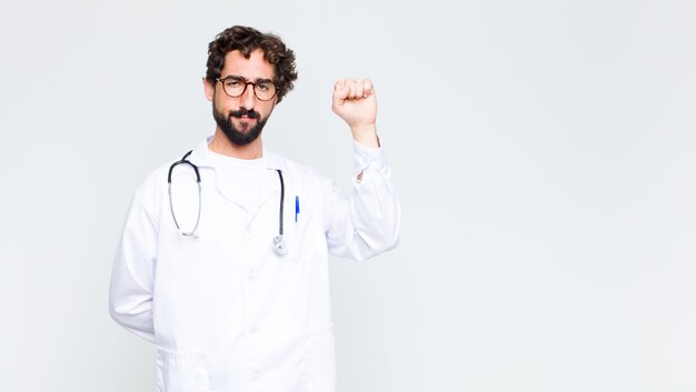 Jeune médecin homme se sentant sérieux, fort et rebelle, levant le poing, protestant ou luttant pour la révolution contre le mur de l'espace de copie