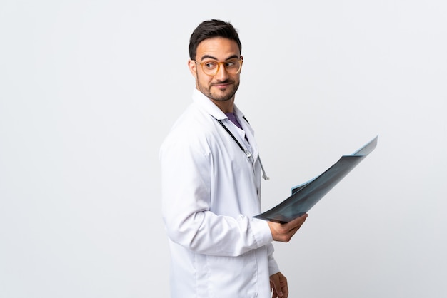 Jeune médecin homme tenant une radiographie isolée sur blanc en riant