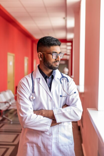 Un jeune médecin indien fatigué ou en pause dans un hôpital covid porte des lunettes et un stéthoscope en blanc