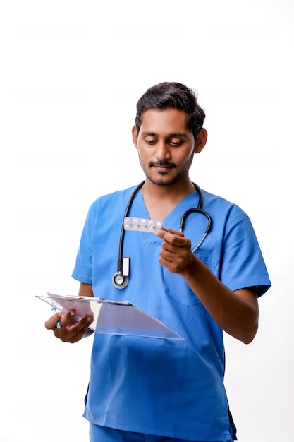 Jeune médecin indien habillé en uniforme avec stéthoscope prenant des notes dans le bloc-notes isolé sur fond blanc.