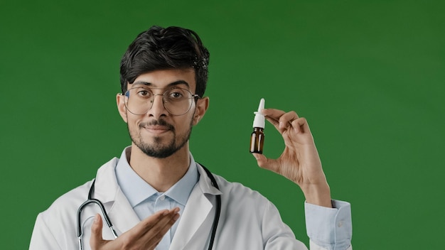 Un jeune médecin indien hispanique arabe en blouse blanche dans un studio vert recommande un spray nasal