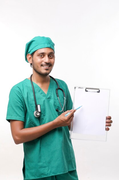 Jeune médecin indien en uniforme avec stéthoscope montrant le bloc-notes sur fond blanc.