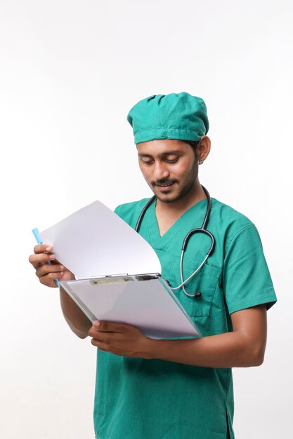 Jeune médecin indien en uniforme avec stéthoscope prenant des notes dans le bloc-notes sur fond blanc.