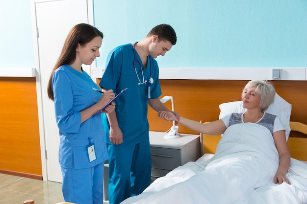 Jeune médecin et infirmière mesurant le pouls et notant les plaintes d'un patient allongé dans le lit d'hôpital de la salle d'hôpital. Concept de soins de santé