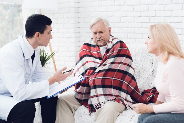 Jeune médecin en manteau visitant un vieux couple à la maison.