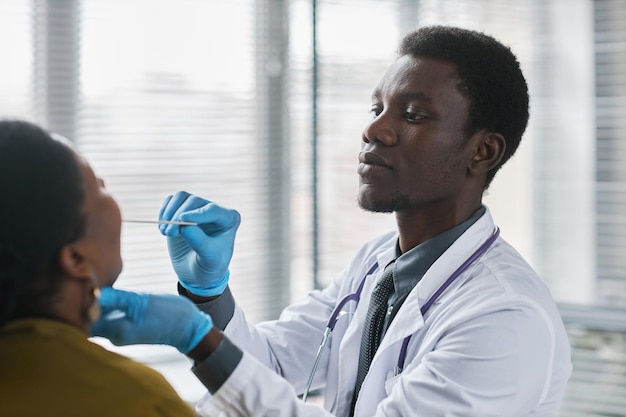 Jeune médecin noir consultant un patient en clinique faisant un examen de la gorge pour la grippe