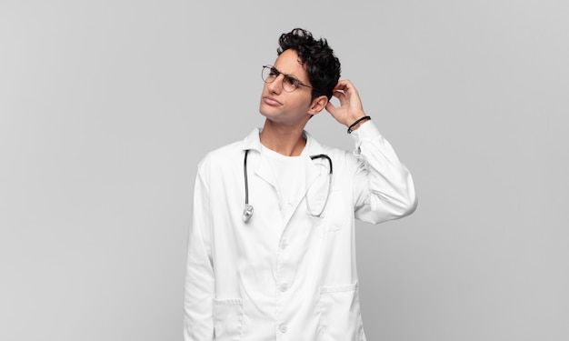 Jeune médecin se sentant perplexe et confus, se grattant la tête et regardant sur le côté