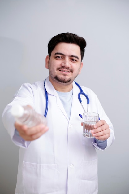 Un jeune médecin se tient debout avec un verre d'eau dans une main et une bouteille d'eau dans l'autre main