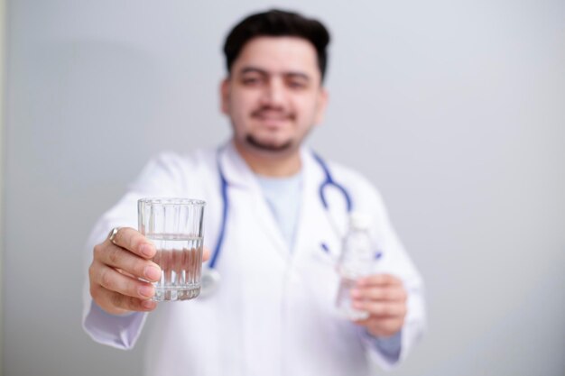 Un jeune médecin se tient debout avec un verre d'eau dans une main et une bouteille d'eau dans l'autre main