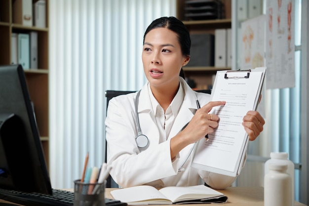 Jeune médecin spécialiste confiant pointant sur le document pendant la consultation