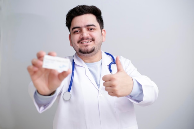 Photo un jeune médecin tient un médicament dans une main et montre un signe de pouce levé