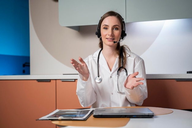 Une jeune médecin en uniforme médical blanc avec un stéthoscope utilisant un ordinateur portable parle via