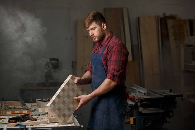 Jeune menuisier avec un tablier dans son atelier