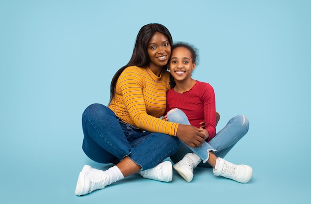 Jeune mère afro-américaine heureuse assise avec sa jolie fille embrassant et souriant à la caméra
