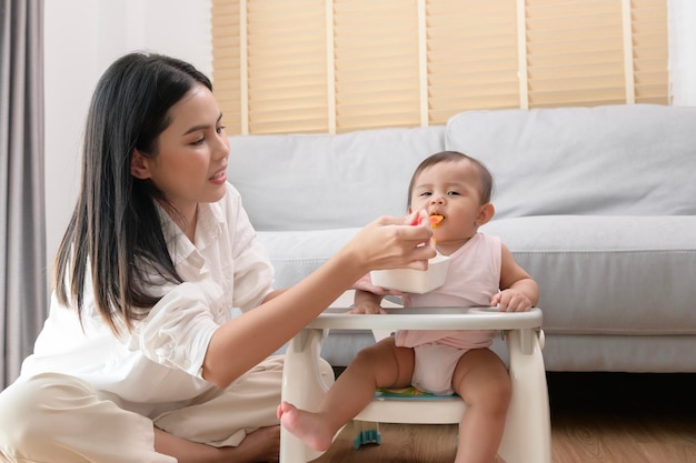 Jeune mère aidant bébé à manger des aliments mélangés sur une chaise bébé