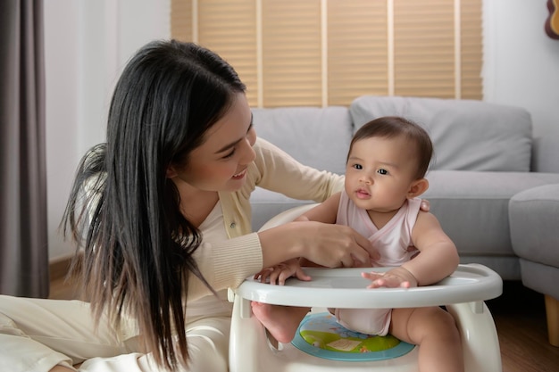 Jeune mère aidant bébé à manger des aliments mélangés sur une chaise bébé