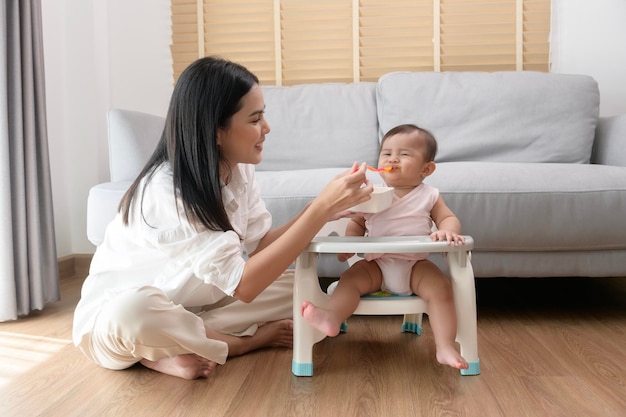 Jeune mère aidant bébé à manger des aliments mélangés sur une chaise bébé