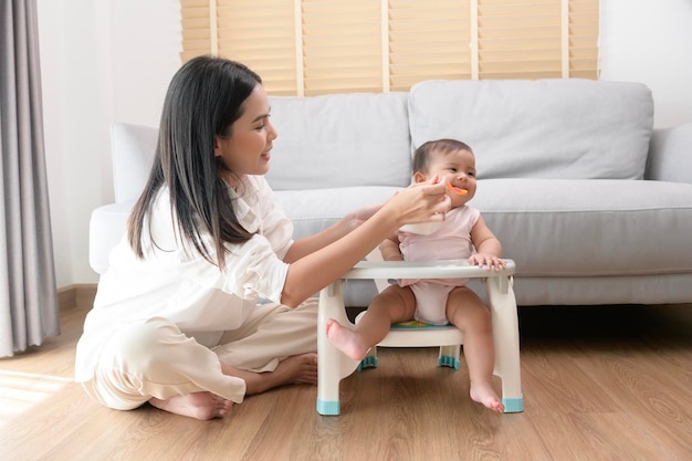 Jeune mère aidant bébé à manger des aliments mélangés sur une chaise bébé