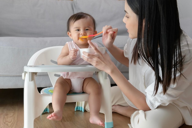 Jeune mère aidant bébé à manger des aliments mélangés sur une chaise bébé