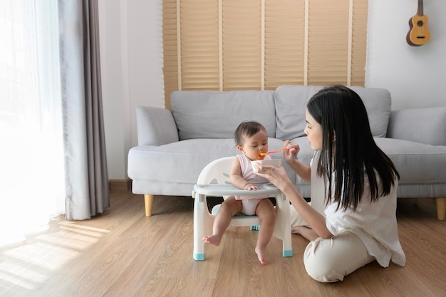 Jeune mère aidant bébé à manger des aliments mélangés sur une chaise bébé