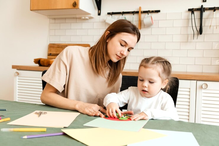 Jeune mère aidant une jolie fille avec un projet d'art et d'artisanat à l'intérieur de la maison La baby-sitter apprend à l'enfant à faire de l'artisanat