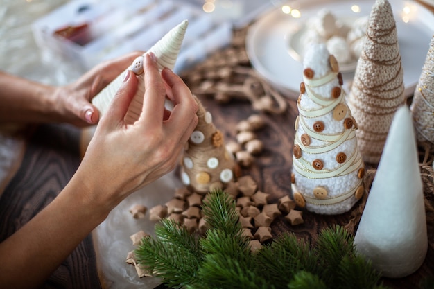 Photo jeune mère aidant sa fille à envelopper le cône de mousse avec de la ficelle ou du fil et à fabriquer des arbres de noël de différentes tailles pour la décoration de table. concept de préparation pour la saison des fêtes et la fête.