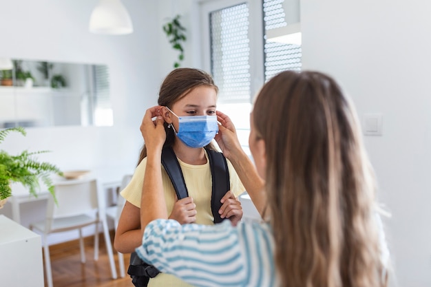 Une Jeune Mère Aide Sa Fille à Porter Un Masque Médical Pour Se Préparer à Aller à L'école. éviter L'épidémie De Covid-19 Ou De Coronavirus. Retour à L'école