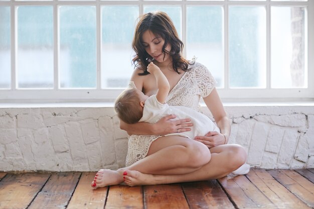 Photo jeune mère allaitant son bébé à la maison dans la salle blanche